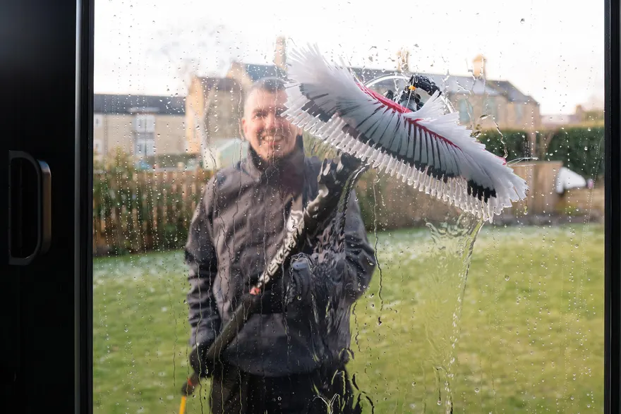 A smiling Tidal cleaner seen through the glass as he cleans it with a pure-water brush