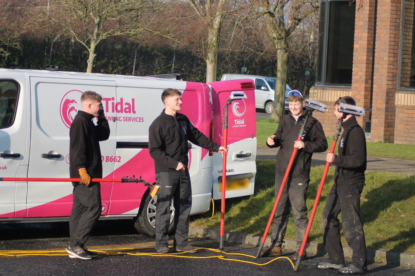 Four Tidal window cleaners with water-fed poles sharing a joke beside a branded Tidal van
